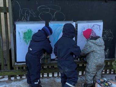 Tre børn der maler udenfor i deres flyverdragt